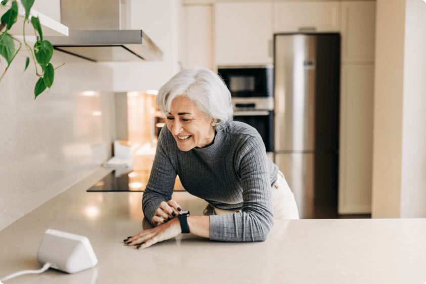 Senior woman in kitchen syncing smart watch to smart clock