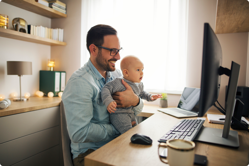 Baby with stunned expression looking at computer screen with smiling man holding him