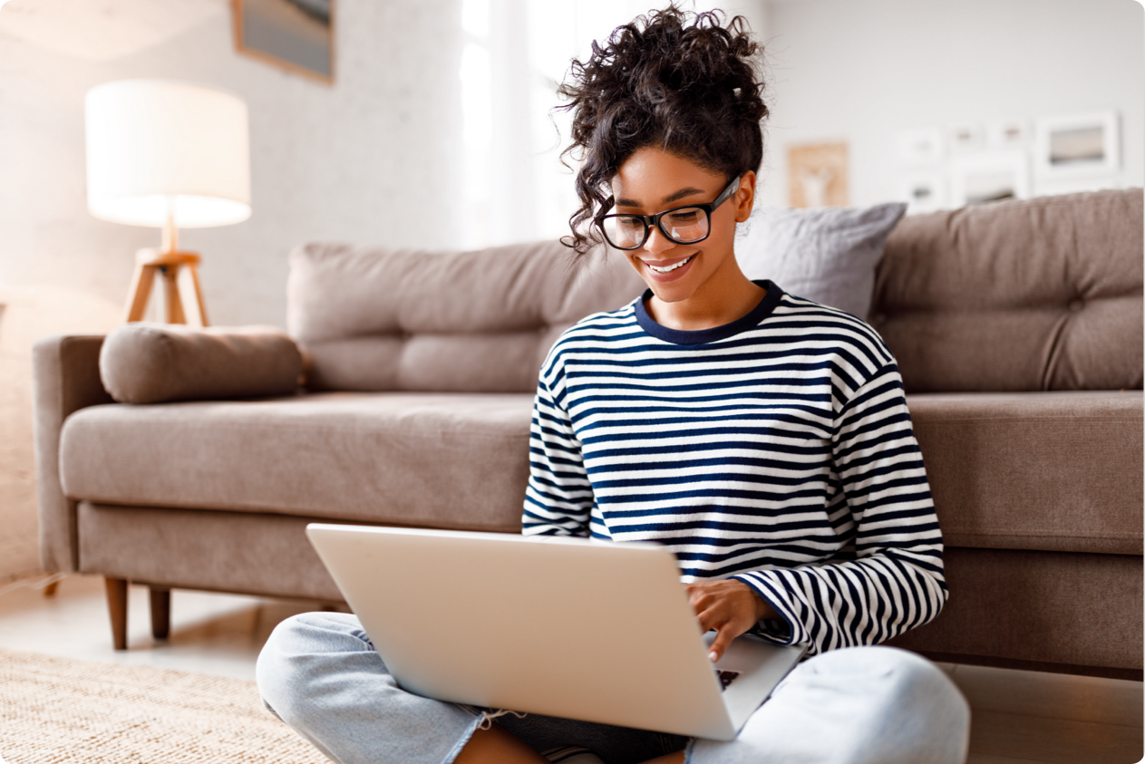 Smiling woman on living room floor looking at her laptop, which is on her lap